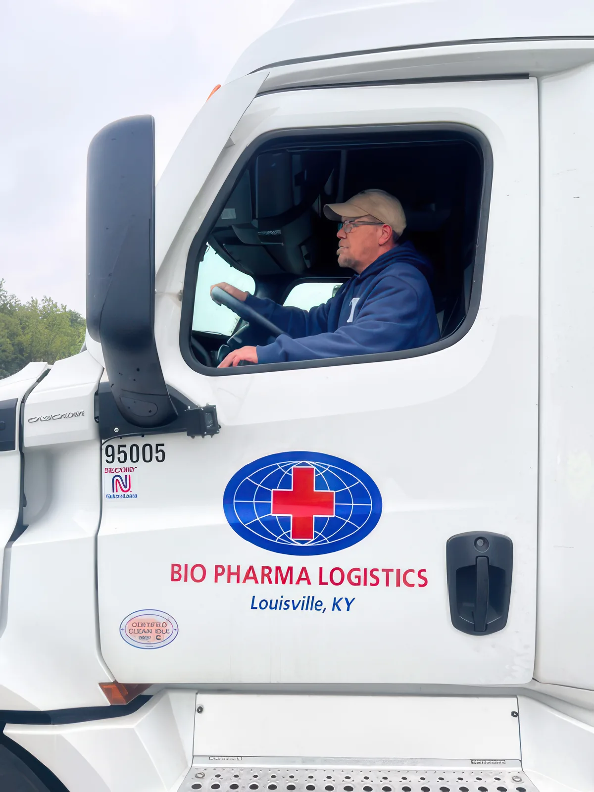 A Bio Pharma Logistics driver at the wheel of a tractor cab, window down and hands on the wheel