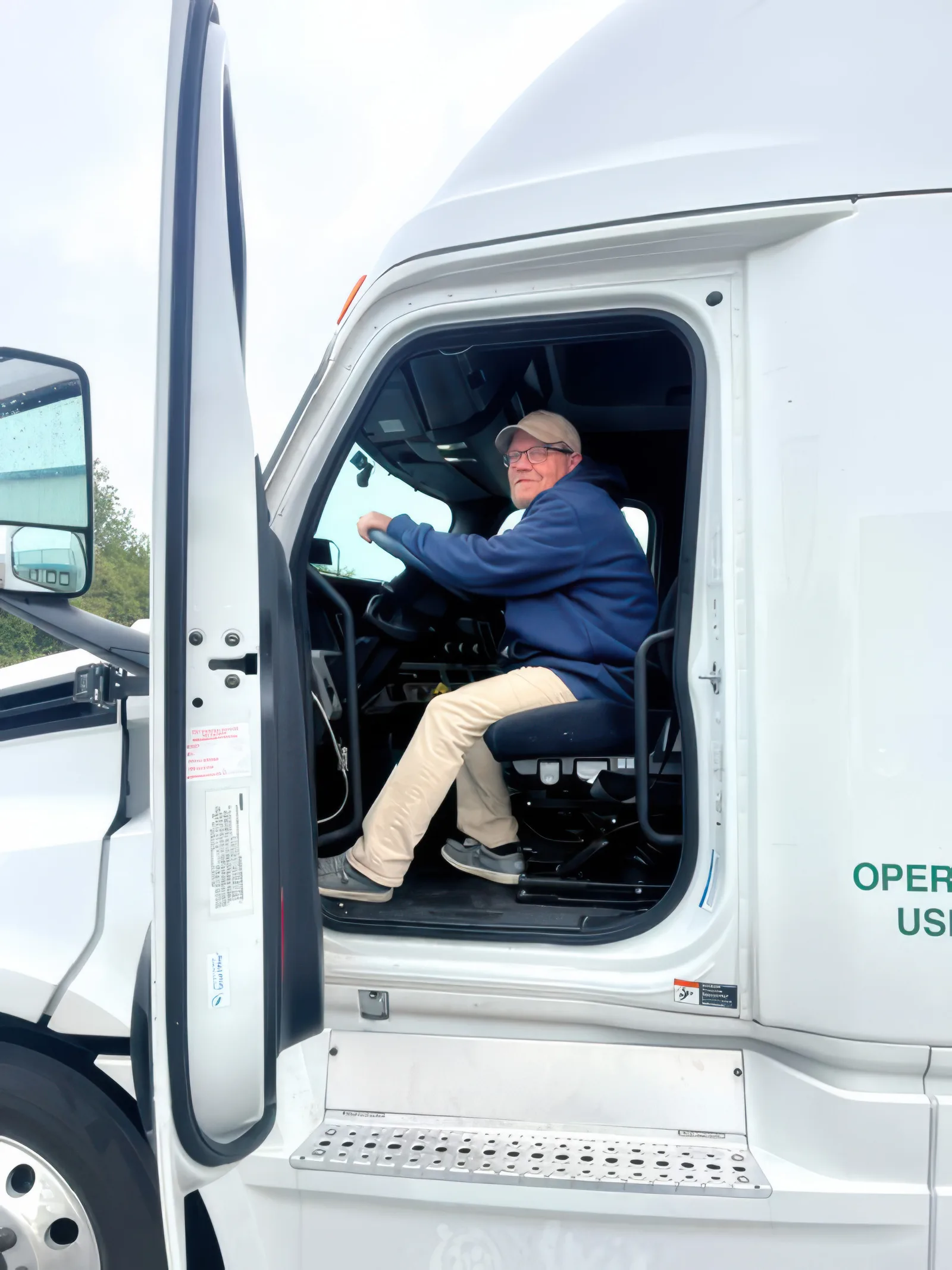 A Bio Pharma Logistics driver seated at the wheel of a tractor with the cab door open, turned toward the camera