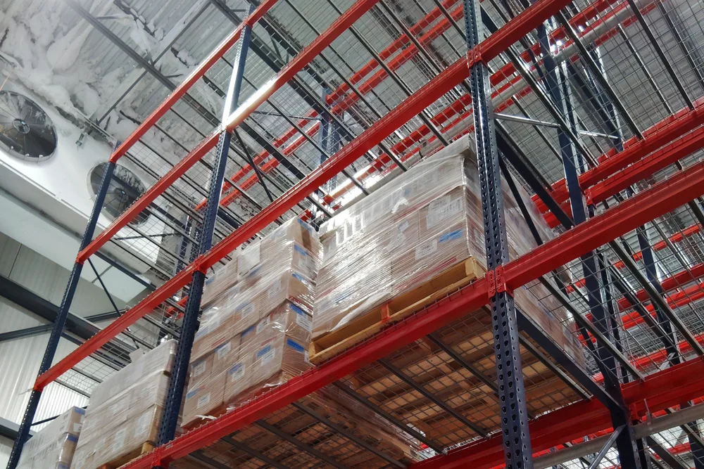 Pallets of cartoned product stored high in the freezer racking at the Louisville facility, with red rack beams and the ceiling structure above